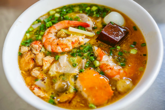 Bức ảnh miêu tả một bát bánh canh cua đầy đặn với sợi bánh canh mềm mại, nước dùng trong vắt và thịt cua tươi ngon, hòa quyện với các gia vị như hành, tiêu, tạo nên một món ăn đầy hấp dẫn.