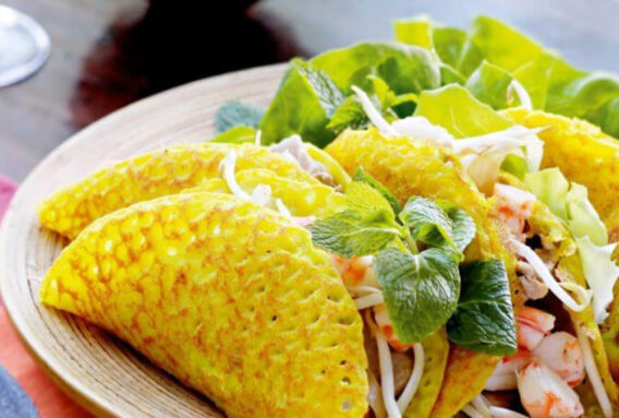 Khám Phá Những Món Ngon Quận 2 Thiên Đường Ẩm Thực Sài Gòn 3 Hình ảnh một chiếc bánh xèo vàng giòn, nhân đầy đủ với tôm, thịt heo, giá đỗ và rau sống được bày biện đẹp mắt trên đĩa. Bên cạnh đó là chén nước mắm chua ngọt đặc trưng để tạo thêm hương vị cho món ăn.